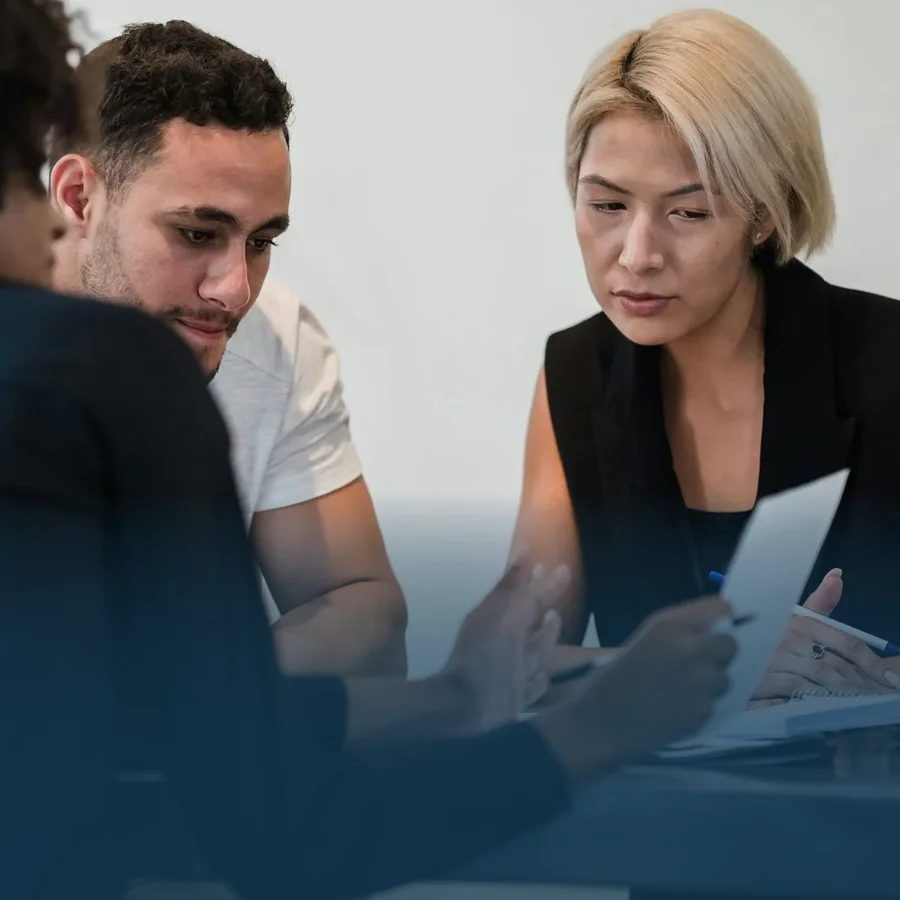 Two individuals consulting with an employee and evaluating a financial sheet.